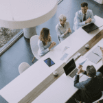 Five professionals meeting in a brightly lit conference room.