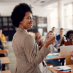 Teacher lecturing in front of a diverse college class. Students listen attentively.