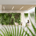 Seated woman on her phone in a waiting room with a lush vertical garden.