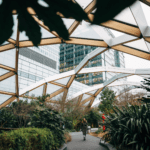 Woman walking through green atrium underneath a skyscraper.