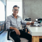 Smiling man with grey hair and glasses at his desk in his office.