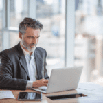 Middle aged man in gray suit sitting at a table on his laptop.