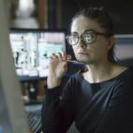 <p>Women diligently looking at computer screen while holding a pen.</p>
